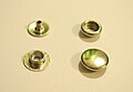 Four pieces of a typical rivet snap fastener: from upper left, the "eyelet" "socket", "cap", and "stud"