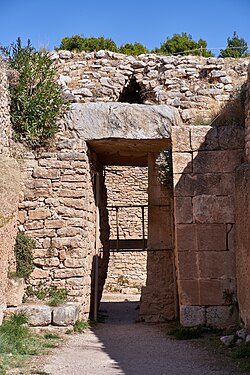 Ancient ruins: a tall rectangular doorway at the end of a broad passageway: the doorway itself is made of large, regular cut blocks; the structures around it of more varied stones.
